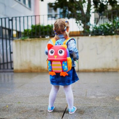 small girl with colourful backpack looks at the entrance to a daycare centre